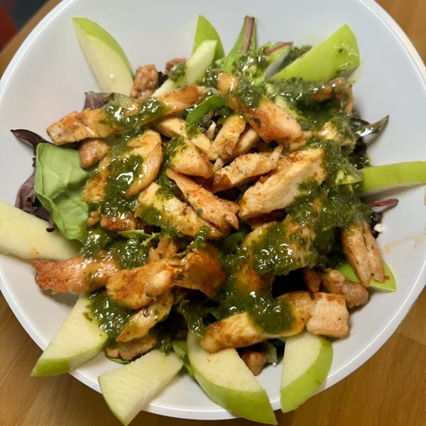 A white bowl filled with grilled chicken strips, green apple slices, and a vibrant green sauce.