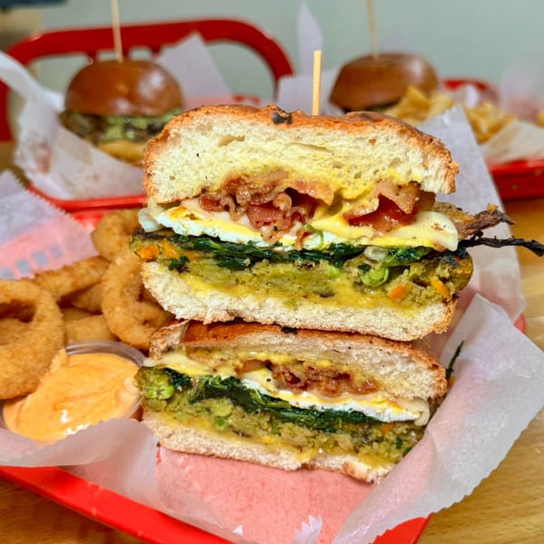 A P.S. Burgers veggie burger, cut in half, with bacon, egg, and onion rings.